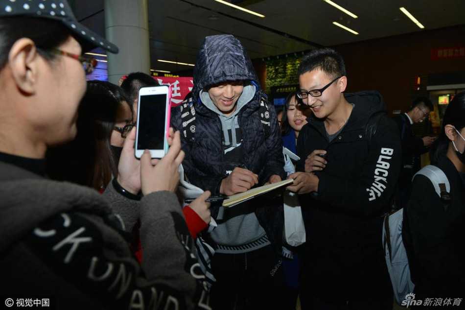 郭艾伦在人群中停下脚步，手持黑色马克笔，正专注地在一位女球迷递来的球衣上留下签名，侧脸轮廓在嘈杂的人群中显得格外认真与暖心。