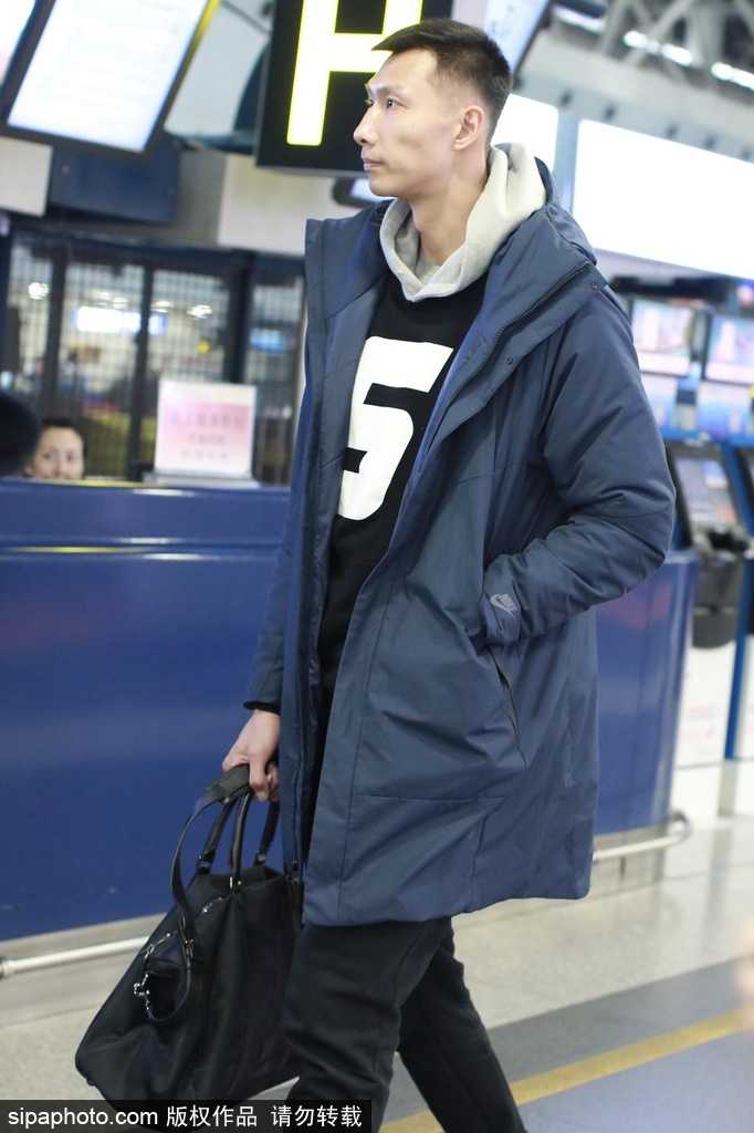 易建联在机场摆渡车上整理衣装，车窗外的光线映照出他专注的神情，时尚与运动在他身上得到了完美融合