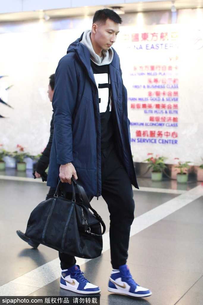 机场大厅内，易建联身着拼接色块潮装侧身而立，轮廓分明，休闲装扮难掩其作为顶级运动员的健硕体型和出众气质