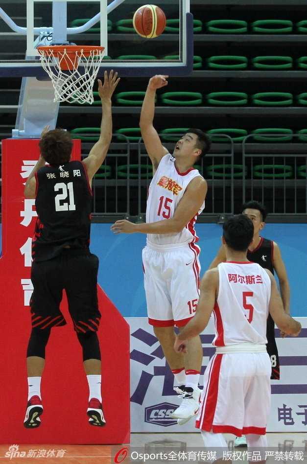 看台上的姚明表情专注而严肃，他庞大的身躯在人群中格外显眼，眼神紧紧跟随着场上飞驰的篮球，仿佛在审视着中国篮球的未来。