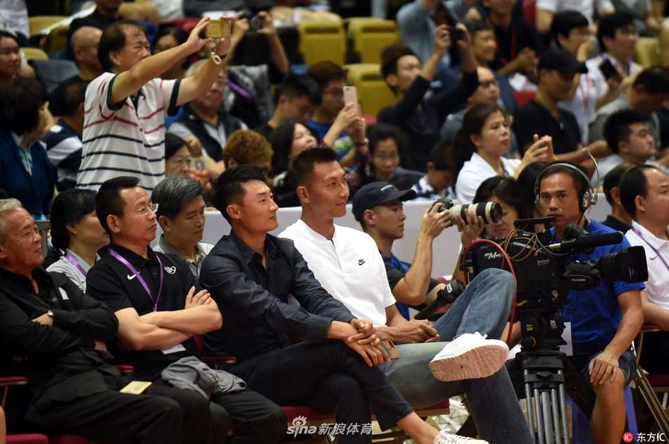 聚光灯下，易建联双手抱在胸前，神情专注地凝视着赛场。身旁的姚明正侧身与友人交谈，而阿联的目光始终追随着场上飞驰的红色身影，眼神里满是对后辈的期许与对中国篮球未来的憧憬。