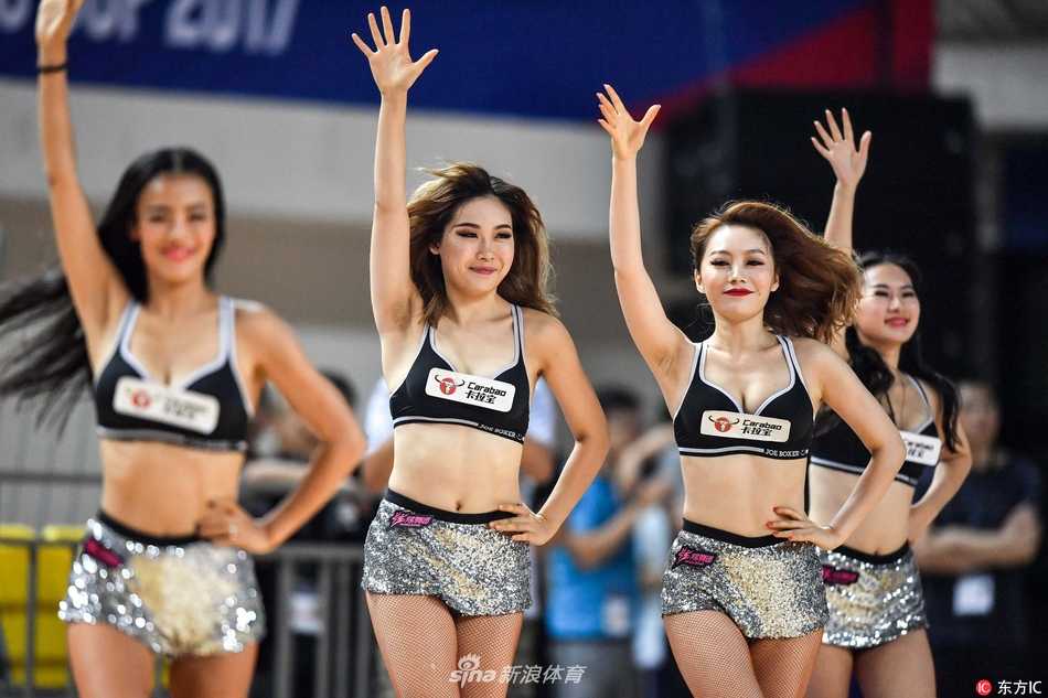 拉拉队员们围成一个小圈，中心一位队员做出高难度的空中劈叉动作，周围的队友们纷纷伸出双手给予保护，展现了团队之间的信任与默契