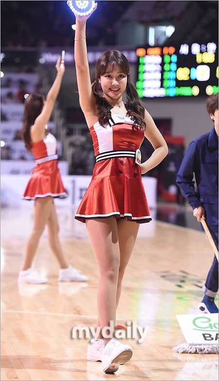 在中场休息的灯光下, 啦啦队员手持彩色花球, 以极具感染力的灿烂笑容面对观众, 展现出阳光健康的形象