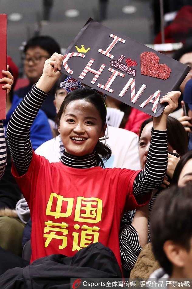 赛场边的看台上，一位身穿应援服的女生回眸一笑，手中紧握着助威旗帜，身后是沸腾的人群，她的眼神明亮而坚定，仿佛在说：这一刻，我与球队同在。