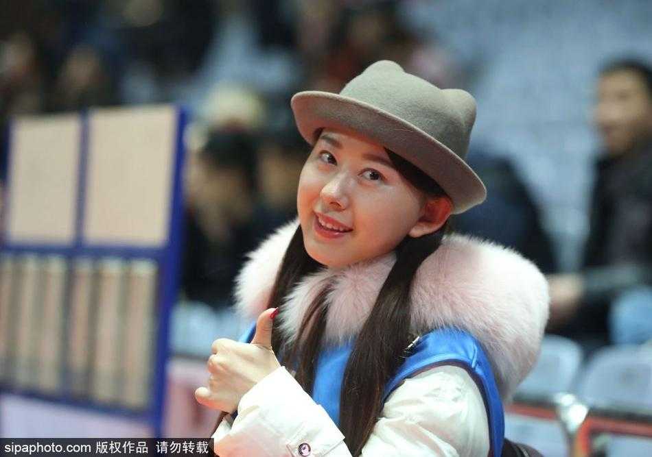 一位衣着时尚的年轻女孩在赛场通道内低头看着手机，身后是已经陆续入场的观众和赛前氛围。她或许是在查看朋友发来的消息，又或者是在浏览关于这场比赛的最新动态，动静之间，自成风景。