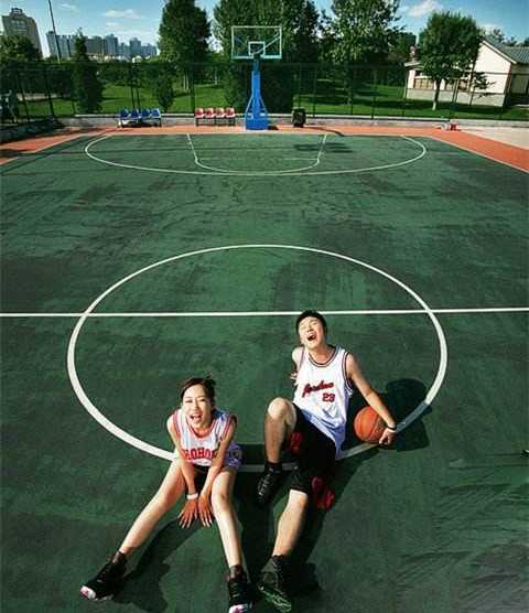 篮球架下的白纱与球衣,这才是爱情最热血的模样 俯拍视角下,新人在巨大的篮球场中线上相对而坐,新娘的婚纱裙摆如花瓣般散开铺陈在地板上,他们正用粉笔写下属于彼此的爱情誓言。