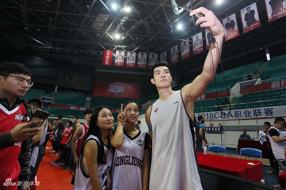 羊城冬日里的热血相聚:广州男篮球迷开放日侧记 广州男篮的多名队员并排坐在场边长椅上,手中拿着签字笔,正在为身前排队的数十名球迷手中的纪念品签名,场面秩序井然。