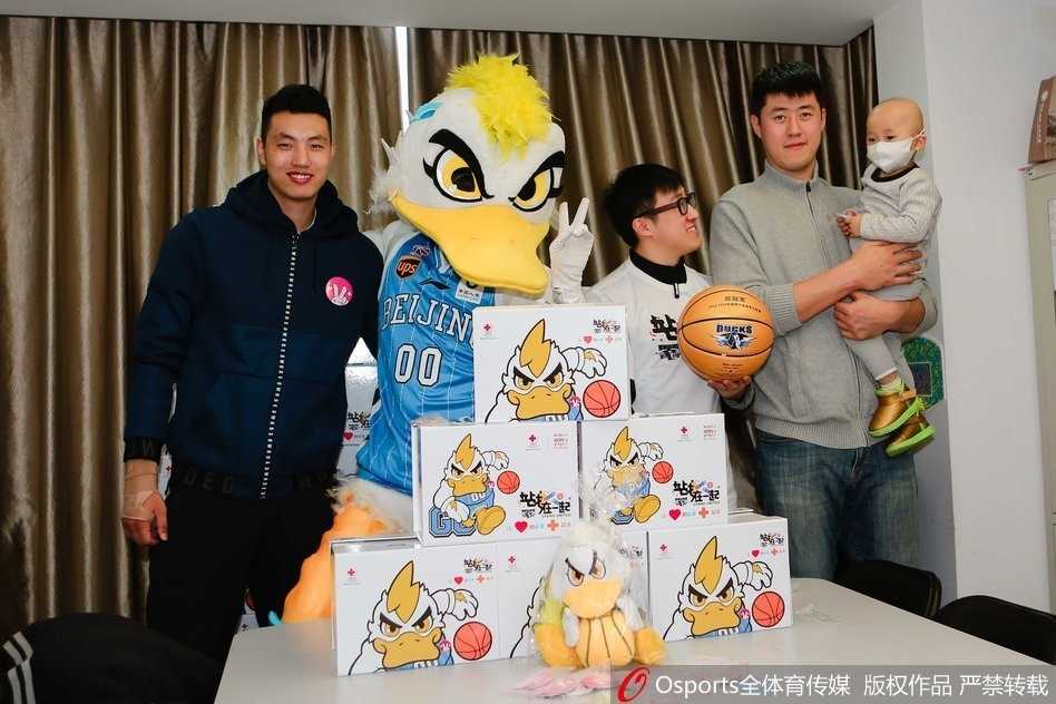 身穿红色队服的翟晓川和张松涛半蹲在病床前，手里拿着彩色画笔，正温柔地与戴着口罩的小朋友一起涂鸦，病床上的小桌板成了临时的画桌，孩子的眼神专注而明亮