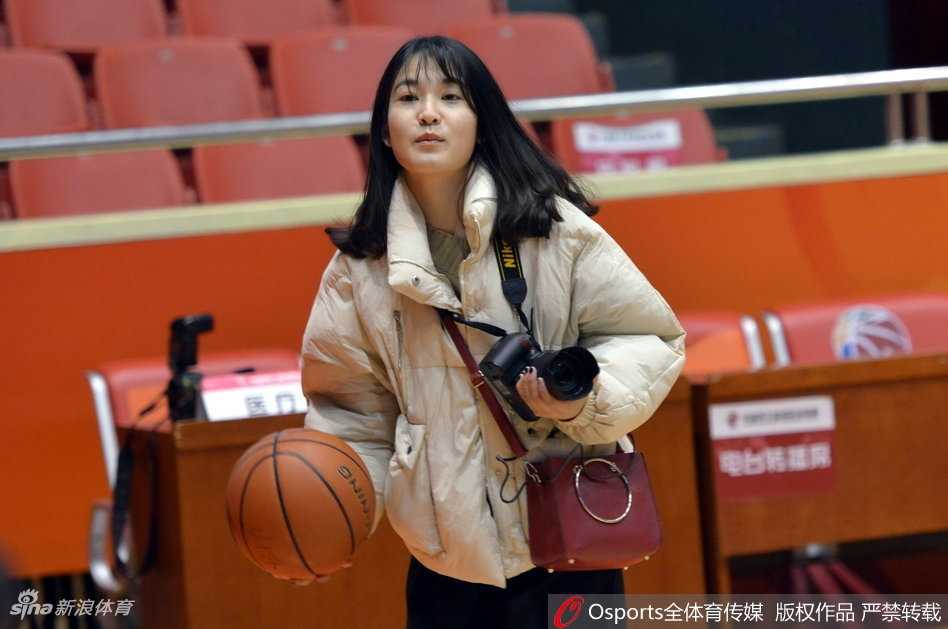 赛场背后探营记:美女记者直击新疆广汇与山东高速男篮高强度备战 训练场全景,两边的篮架下分别摆放着新疆和山东队的训练用球。美女记者背对镜头,提着采访包正走向出口,整个球馆在灯光照射下显得格外庄重,一天的探营报道圆满结束。