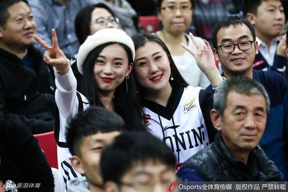 远征的赤木晴子:辽宁男篮的美女球迷客场闪耀记 一位戴着眼镜、学生气质的辽宁美女球迷,高举着加油的手势,眼神坚定地望向赛场方向,全身心投入为辽篮助威。