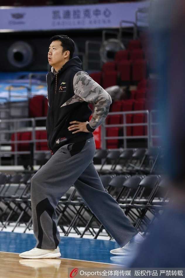 王治郅在训练中弯腰屈膝，做出扎实的防守滑步动作，他眼神坚毅地盯着前方持球的年轻队员，用身体力行告诉后辈什么才是八一队的铁血防守。