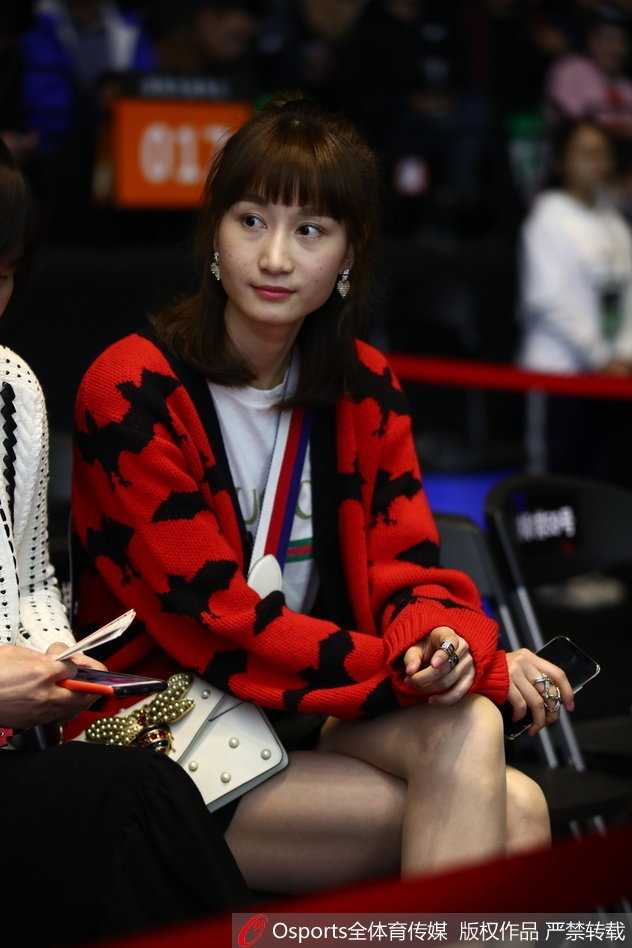 太太团成员之一在场边专注地观看比赛，手中拿着CBA官方应援棒，脸上洋溢着开心的笑容，完全沉浸在比赛的紧张与欢乐氛围中。