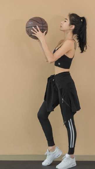 双手抱球的她站在三分线外，目光如炬地凝视着篮筐。紧身的运动背心勾勒出她纤细有力的腰肢，修长的双腿充满力量感，随时准备启动突破。