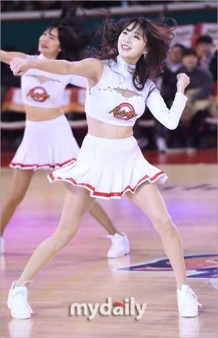 鏡頭捕捉到一位正專注熱舞的啦啦隊員，她身著黑色運動背心，露出健康的小麥色肌膚。隨著強烈的節奏甩動長髮，舉手投足間散發著青春陽光的活力與熱情。