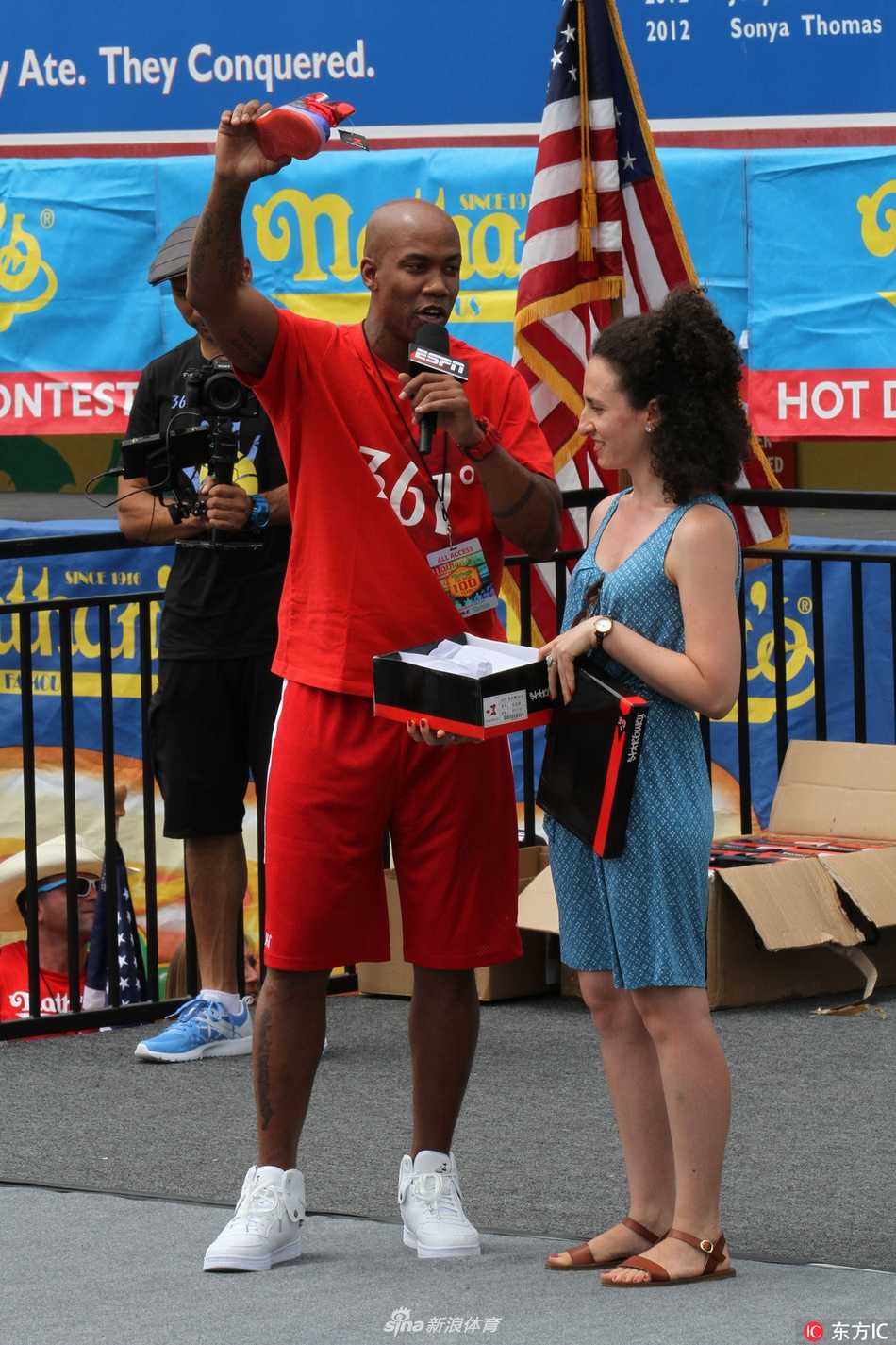 镜头拉近，马布里神情专注地看向比赛方向，左手下意识地指向自己胸前那个醒目的个人品牌商标，仿佛在告诉镜头后的观众：今天的主角除了热狗，还有我脚下的这双鞋。